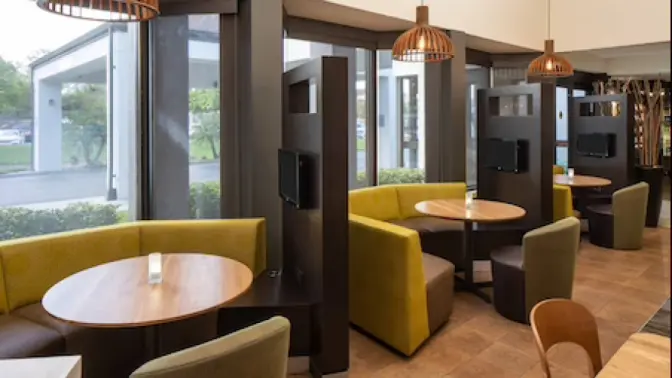 Courtyard by Marriott hotel dining area, featuring three cozy booths with green upholstery, circular tables and modern light fixtures.