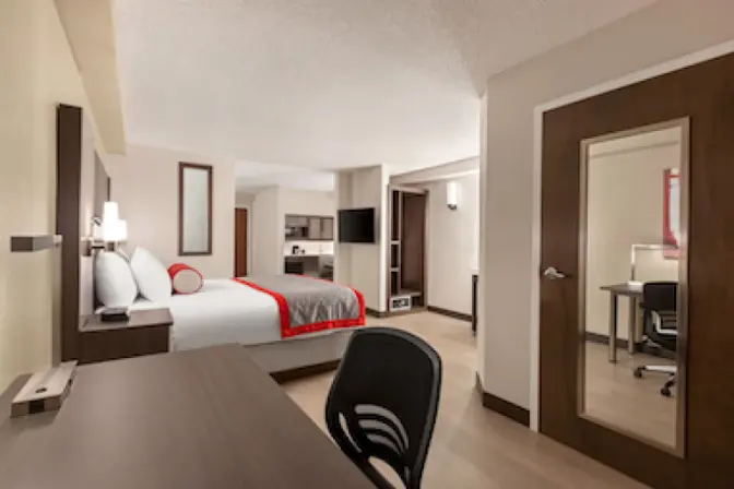 Modern king room at Ramada Suites featuring a comfortable king sized bed a kitchenette and a desk.