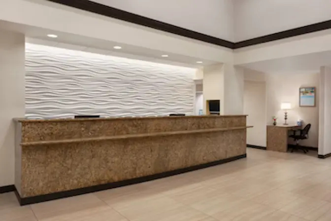 Elegant lobby area of Ramada Suites, showcasing a spacious layout with a sleek reception desk, and tasteful decor under warm, ambient lighting.
