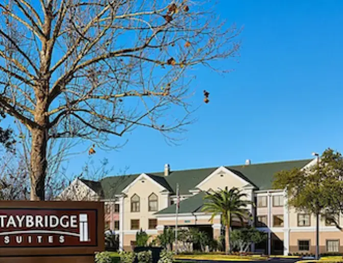 Staybridge Suites Orlando International Airport Hotel building with a large sign in the foreground and a clear blue sky above.