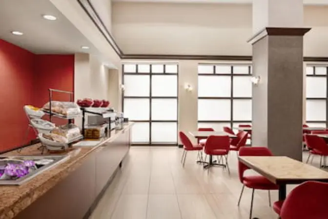 Spacious and stylish dining space at Ramada Suites, showcasing a variety of seating arrangements, sleek wooden tables, ambient lighting, and large windows providing a bright, airy atmosphere.