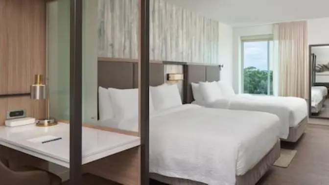 Spacious hotel room with two queen beds, featuring a modern design with a soft color palette and large windows providing natural light.