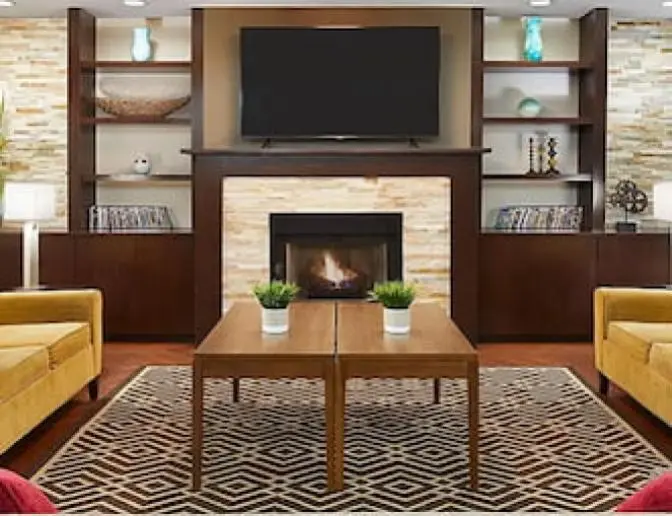 Modern lobby at Staybridge Suites Orlando International Airport Hotel with comfortable yellow armchairs, a fireplace, and a TV, accented by stylish decor."