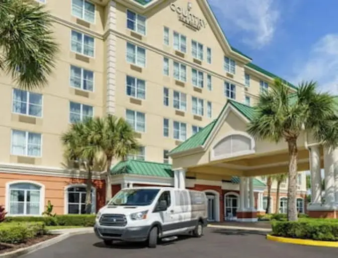 Country Inn & Suites near Orlando Airport, featuring a grand entrance with palm trees and manicured lawn against a warm evening sky.