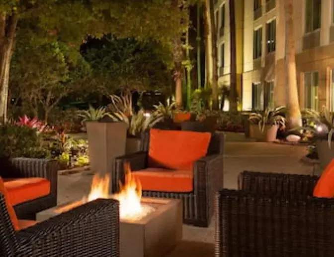 Evening view of a courtyard at the Hilton Garden Inn Orlando Airport Hotel with comfortable wicker seating and a central fire pit surrounded by lush greenery.