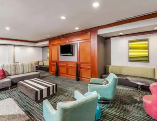 Lobby seating area at Residence Inn by Marriott featuring a mix of colorful chairs, striped coffee table, sectional sofa with decorative pillows, and a wall-mounted TV surrounded by wooden paneling.