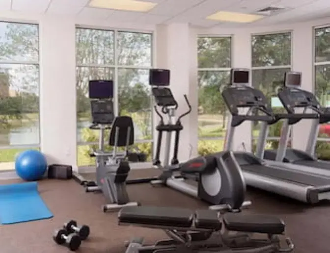 Gym area at SpringHill Suites by Marriott equipped with cardio machines, including treadmills and an elliptical, as well as a yoga mat, free weights, and an exercise ball, with floor to ceiling windows.