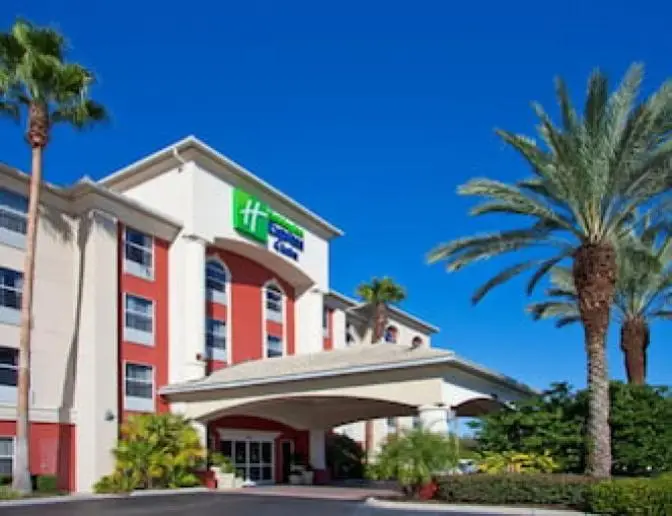 Exterior view of Holiday Inn Express Orlando International Airport Hotel, featuring a bright terracotta and beige building with tall palm trees displayed against a bright afternoon sky.