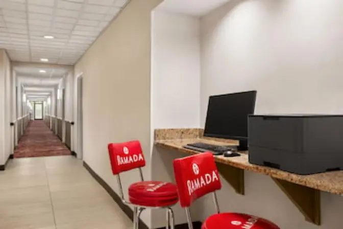 Functional business center at Ramada Suites, equipped with several workstations, comfortable seating, desktop computers, and a printer, offering a professional and efficient workspace.
