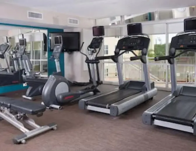 Hotel fitness center at Residence Inn by Marriott showcasing treadmills, elliptical machines, a stationary bike, and a weight bench, with large mirrors reflecting the equipment.