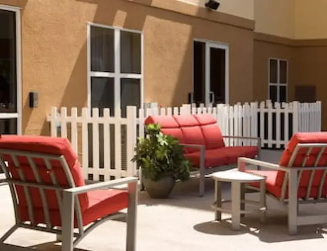 Comfortable outdoor seating at Residence Inn by Marriott, showcasing red cushioned chairs, a sofa, a small table, and white picket fencing on the patio.
