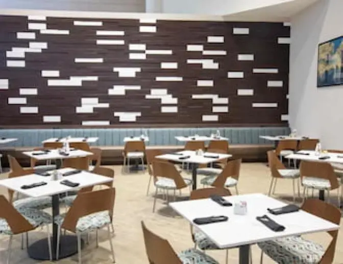 Holiday Inn Orlando International Airport hotel dining area with wooden chairs, white tables, and a modern geometric wall design.