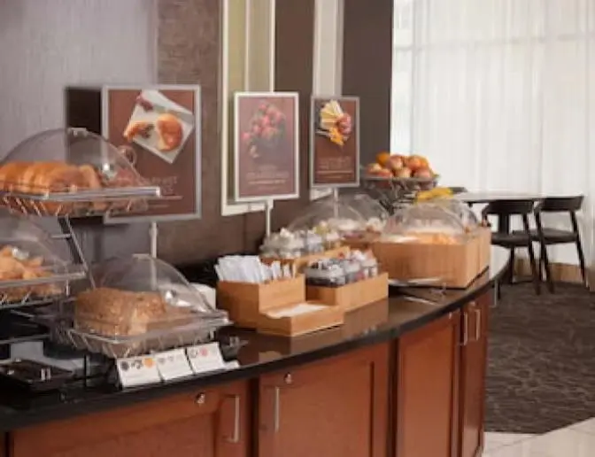 Continental breakfast station at SpringHill Suites by Marriott featuring trays of pastries, fresh fruit, sliced meats and cheeses, bread, and various condiments.
