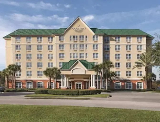 Country Inn & Suites near Orlando Airport, featuring a grand entrance with palm trees and manicured lawn against a warm afternoon sky.