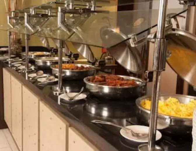 Breakfast buffet with a selection of hot items including scrambled eggs, sausages, and breakfast potatoes, served in covered trays.