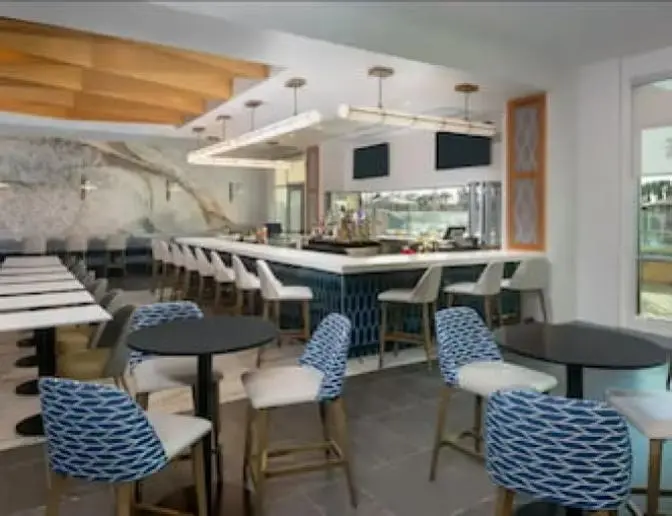 Bright modern dining area inside Hyatt House Hotel near Orlando International Airport featuring bright orange and wood wall and ceiling accents with high top bar seating.