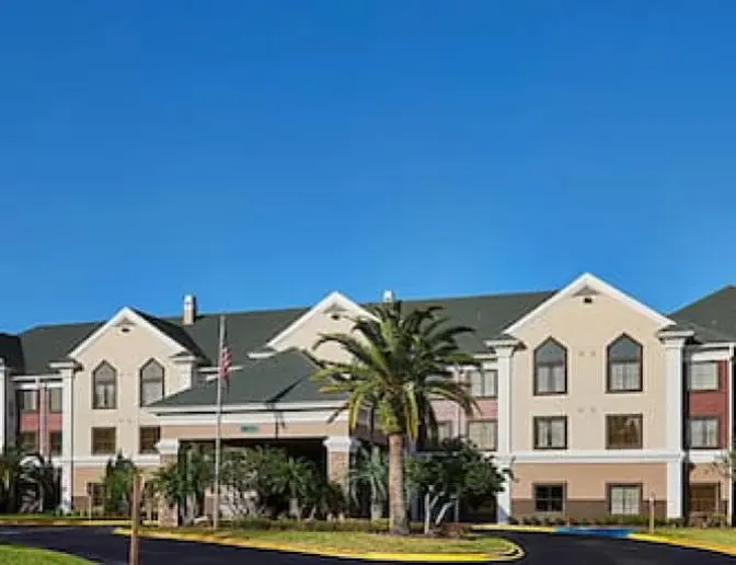 Exterior of Staybridge Suites Orlando International Airport Hotel, showcasing the main building, driveway, and surrounding greenery.