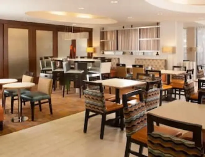 A modern dining area with a mix of tables and chairs, featuring a blend of wood and patterned upholstery. The room has warm lighting and a contemporary design with wooden partitions and a variety of seating options, including high chairs and cushioned seats.