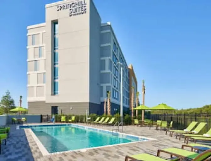 Outdoor pool area at SpringHill Suites featuring lime green lounge chairs, umbrellas, and a clean, rectangular pool under a clear blue sky.