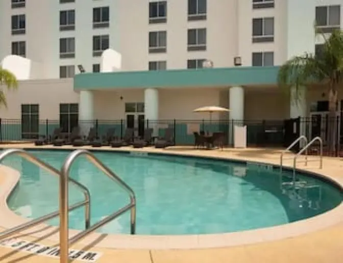SpringHill Suites by Marriott outdoor pool area featuring a clear blue pool, sun loungers, umbrellas, and palm trees, with the hotel building in the background.