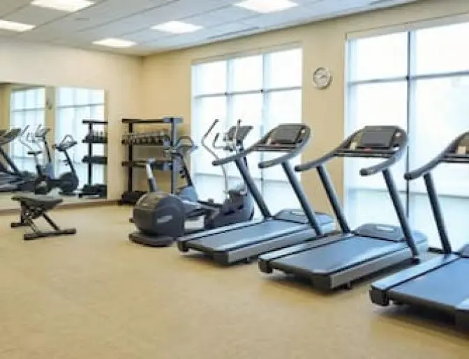 Modern fitness room at SpringHill Suites Lake Nona, equipped with treadmills, stationary bikes, and a free weight area, offering ample light from large windows.