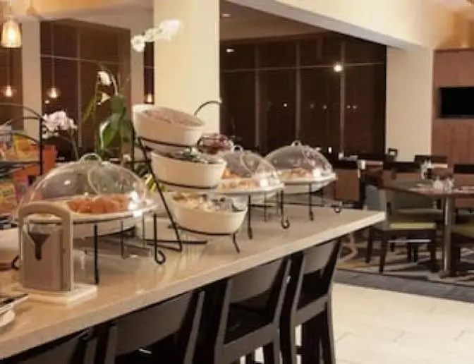 Hilton Garden Inn Orlando Airport Hotel dining room showcasing a breakfast buffet with an assortment of cereals, pastries, and fresh fruit, along with elegant lighting and seating.