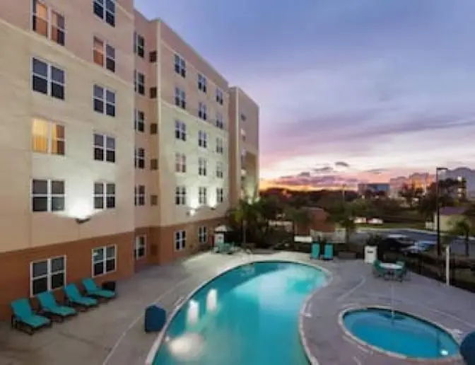 Outdoor pool area at Residence Inn by Marriott at dusk, with the hotel building illuminated, featuring a swimming pool, hot tub, lounge chairs, and a beautiful sunset in the background.