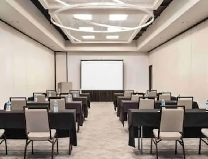 Holiday Inn Orlando International Airport conference room setup with tables and chairs, featuring a projector screen at the front and a stylish circular ceiling light fixture.