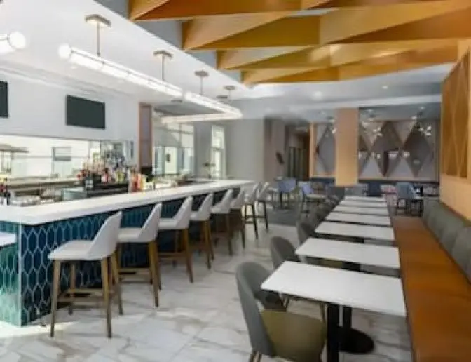 Bright modern dining area inside Hyatt House Hotel near Orlando International Airport featuring bright orange and wood wall and ceiling accents with high top bar seating.