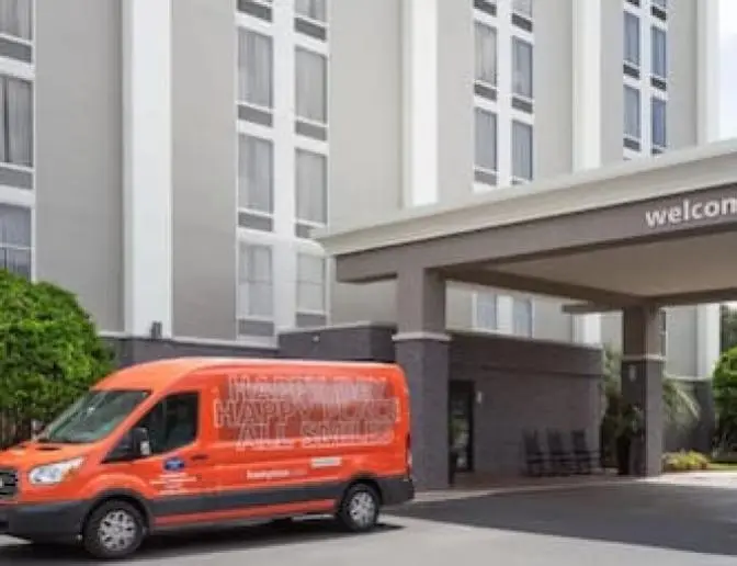 Hampton Inn Orlando International Airport Hotel entrance featuring a welcoming sign and an orange shuttle van.