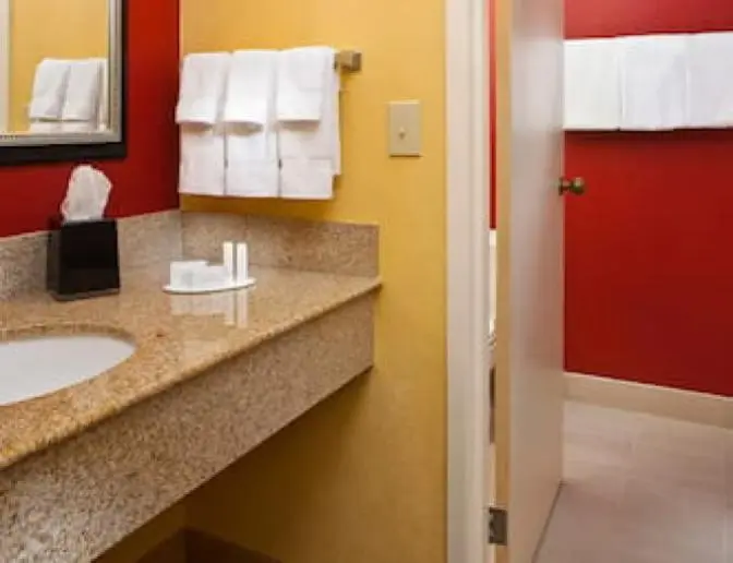 Bathroom at the Courtyard by Marriott featuring a granite countertop with a sink, a large mirror, and neatly arranged towels on a towel rack.