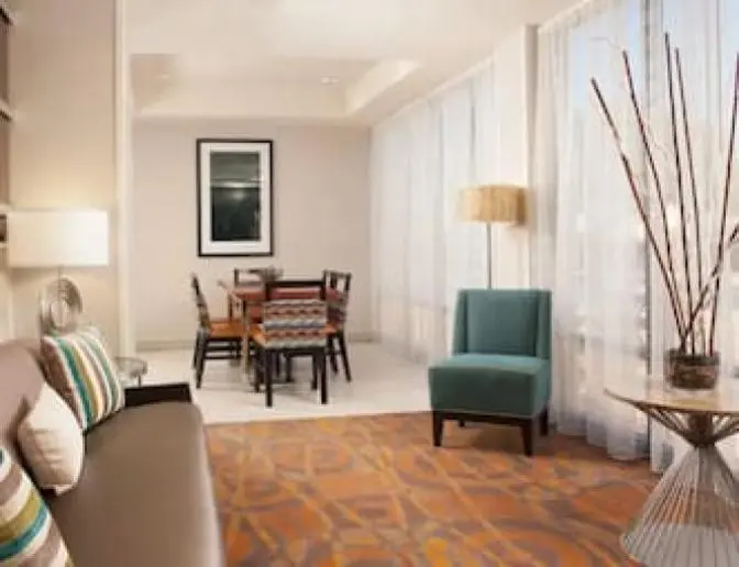 Hampton Inn Orlando International Airport Hotel lobby seating area featuring a cozy sofa with colorful pillows, a round table with decorative branches, and a dining table set.