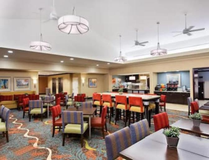 Large dining area inside Homewood Suites by Hilton near Orlando Airport featuring vibrant patterned chairs and carpeting with plenty of seating options.