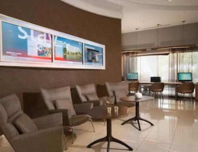Interior view of SpringHill Suites by Marriott lobby, highlighting a modern seating area with gray chairs, a digital display board, and a business center with computers for guest use.