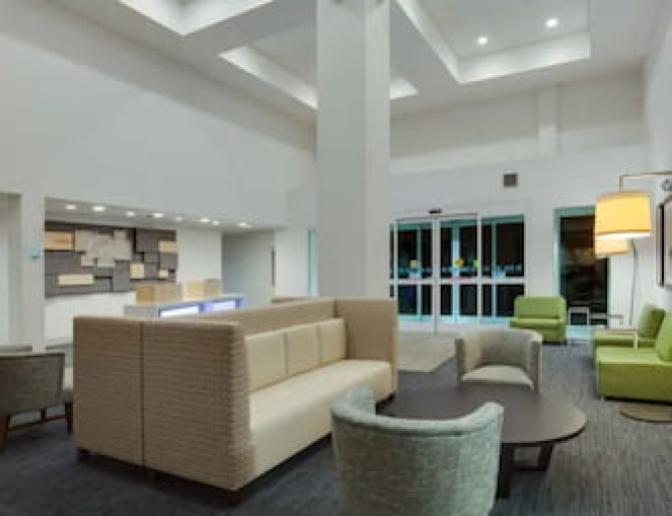 Holiday Inn Express Orlando International Airport Hotel lobby sitting area featuring multiple tan couches, green chairs and modern geometric art.