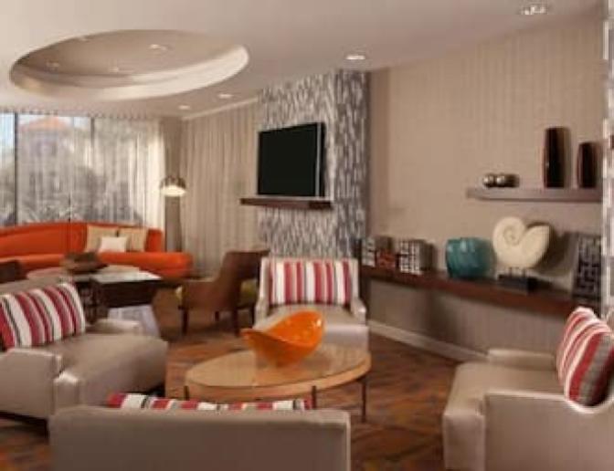 Contemporary lobby at Hampton Inn Orlando International Airport Hotel featuring a round orange sofa, armchairs with striped pillows, and modern decor elements.