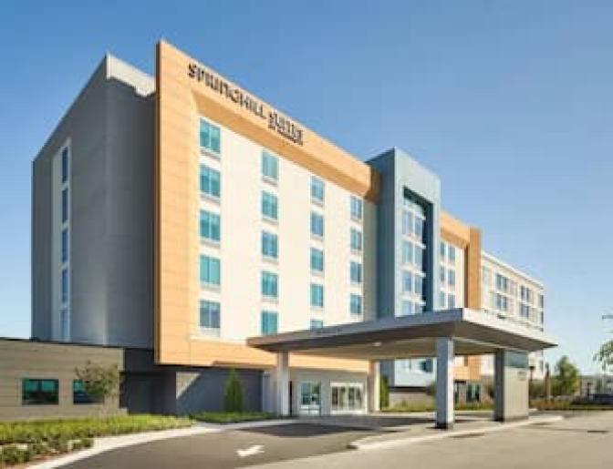 SpringHill Suites by Marriott in Lake Nona, showcasing a modern facade with beige, blue, and orange accents, and a convenient front drive-through entrance.