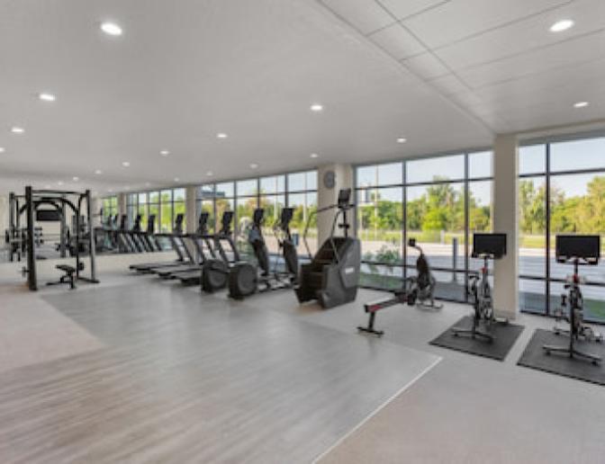 EVEN Hotel's fitness center featuring treadmills, stationary bikes, stair climbers, and resistance training equipment, with floor-to-ceiling windows offering scenic views of surrounding greenery.