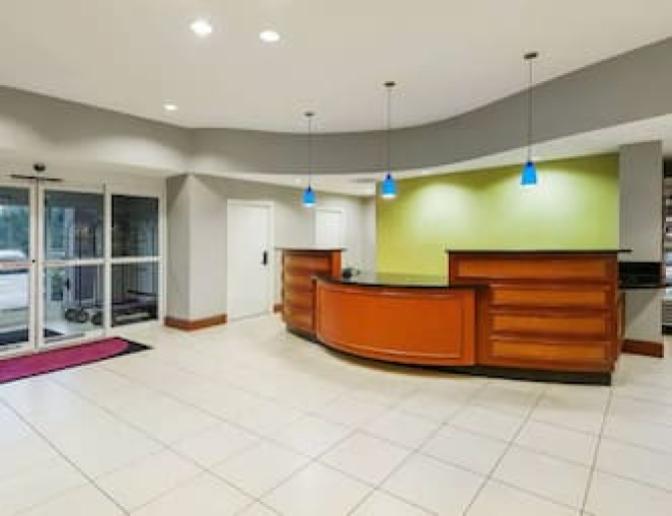 Reception area at Residence Inn by Marriott with a curved wooden front desk, blue hanging lights, green accent wall, and glass doors leading to the outside.