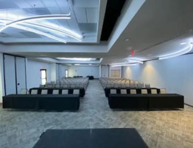 Spacious conference room set up in classroom style with rows of chairs and tables, featuring modern lighting and a neutral color scheme.