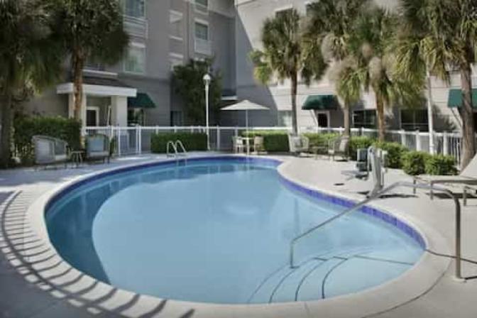 Outdoor swimming pool in the courtyard of Homewood Suites by Hilton near Orlando Airport surrounded by grey pool lounge chairs and tables.