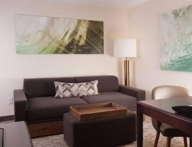 Two Queen bedroom at SpringHill Suites by Marriott featuring a gray sofa with decorative pillows, a wooden coffee table, a standing lamp, and wall art with green and white abstract designs.