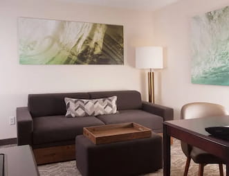 Two Queen bedroom at SpringHill Suites by Marriott featuring a gray sofa with decorative pillows, a wooden coffee table, a standing lamp, and wall art with green and white abstract designs.