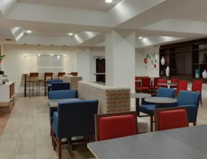 Warm spacious dining area inside Holiday Inn Express Orlando International Airport Hotel  featuring res and blue chairs and geometric patterned booths.