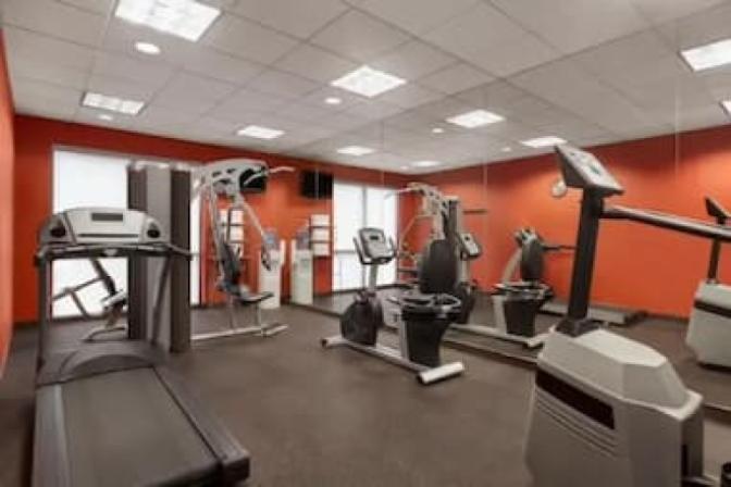 Ramada Suites fitness center featuring a variety of modern exercise equipment, including treadmills, stationary bikes, free weights, and large mirrors on the walls for an open and spacious feel.