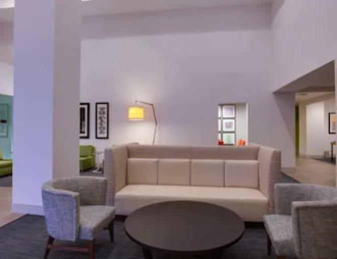 Holiday Inn Express Orlando International Airport Hotel spacious lobby sitting area featuring a tan couch with two grey chairs surrounding a circular coffee table.