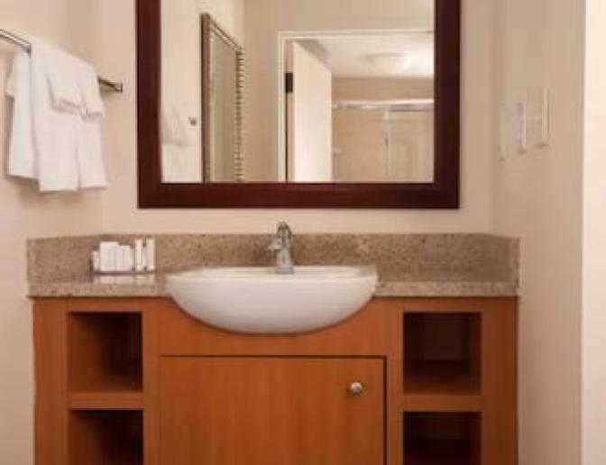 Bathroom vanity at SpringHill Suites by Marriott featuring a granite countertop, modern sink, wooden cabinetry, a large mirror, and neatly arranged toiletries.