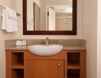 Bathroom vanity at SpringHill Suites by Marriott featuring a granite countertop, modern sink, wooden cabinetry, a large mirror, and neatly arranged toiletries.