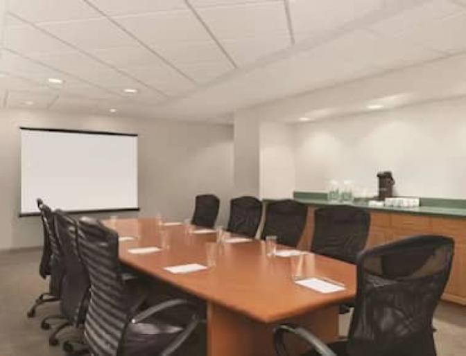 Multipurpose business center conference room featuring a large conference table, rolling chars and a projector with a screen.