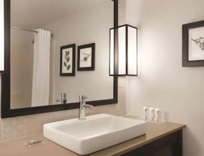 Modern bathroom inside a bedroom at the Country Inn & Suites near Orlando Airport featuring a mosaic tile backsplash and large mirror.